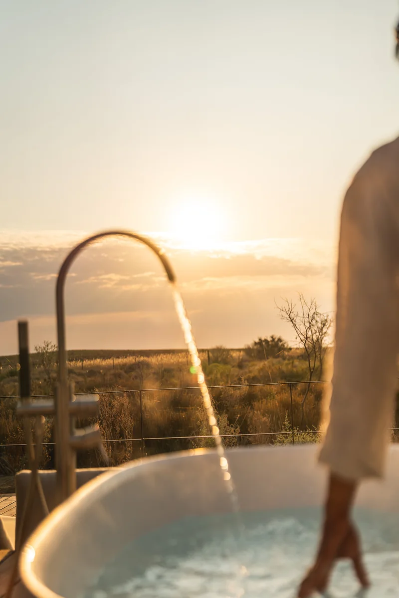 A hand trailing through a bath as it fills at sunset